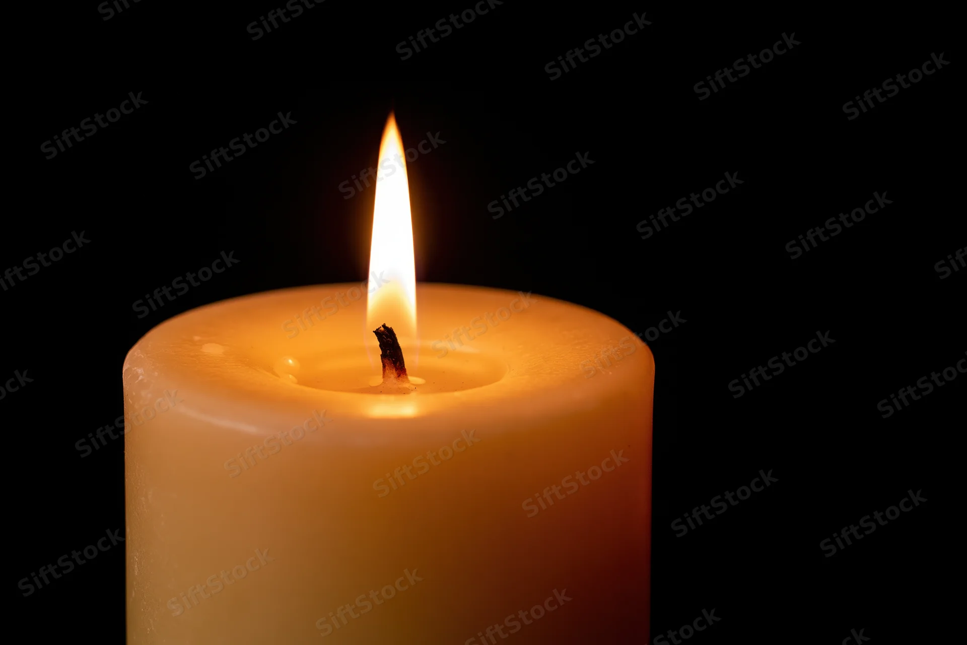 Thick pillar candle burning steadily with upright flame against black background