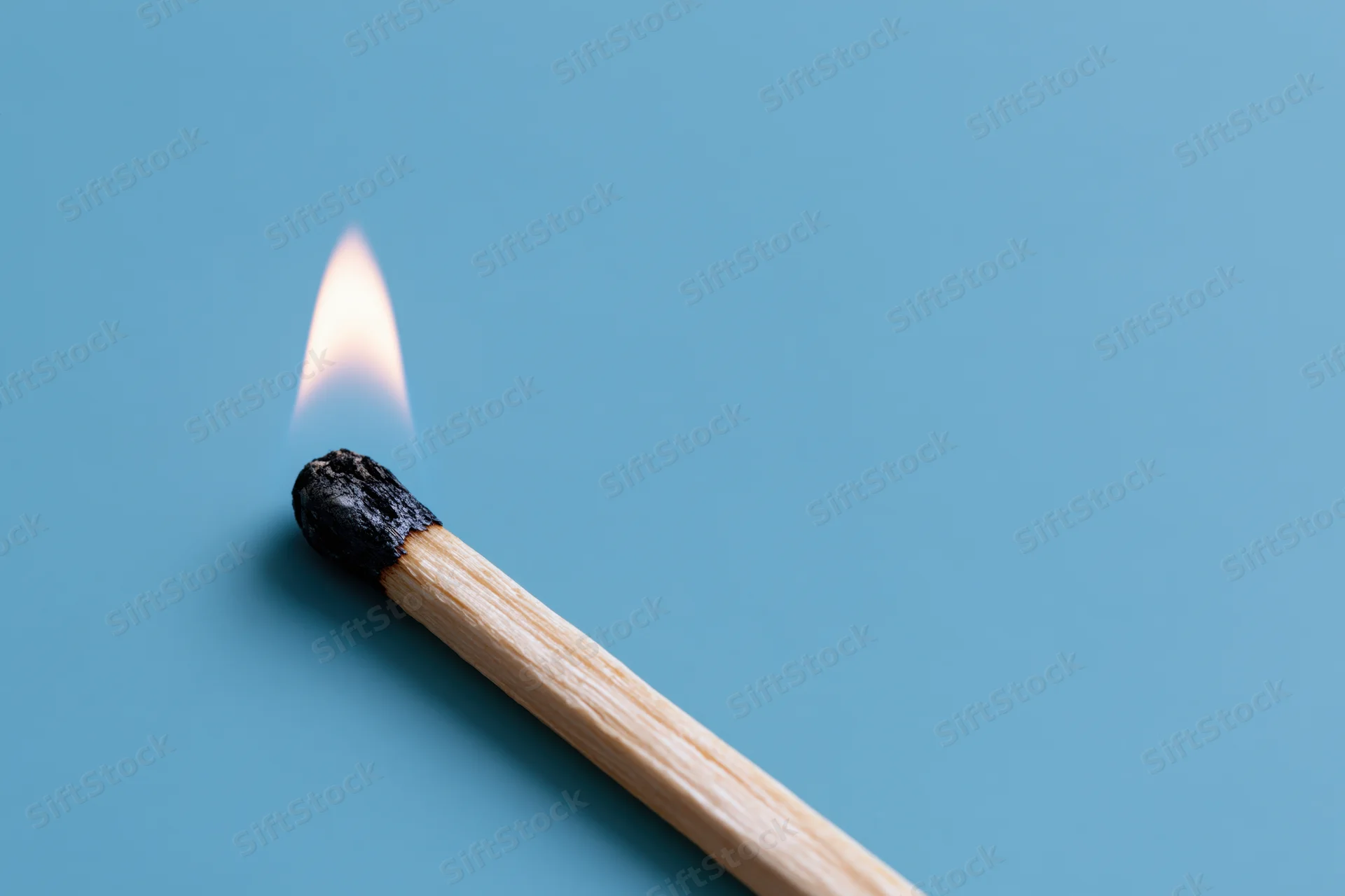 Burning wooden matchstick with small pale flame on blue background