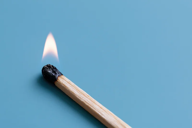 Burning wooden matchstick with small pale flame on blue background