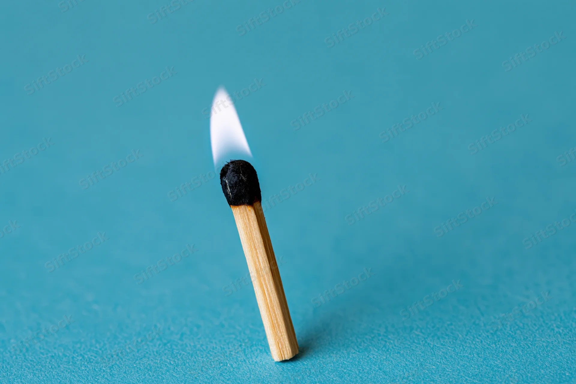 Single wooden matchstick burning with a small pale flame on a blue background