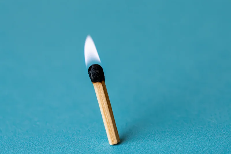 Single wooden matchstick burning with a small pale flame on a blue background