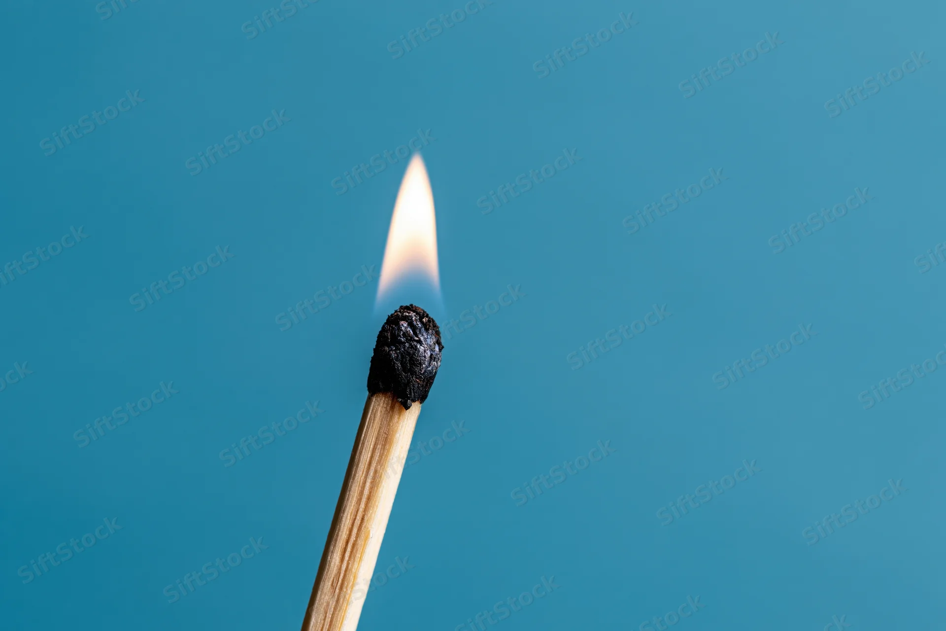 Burning matchstick with flame against blue background