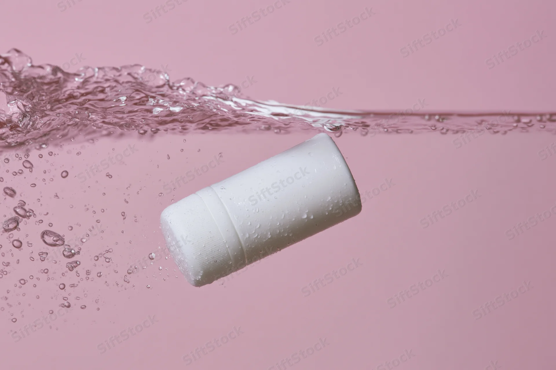 White roll-on deodorant bottle floating just below water surface against pink background