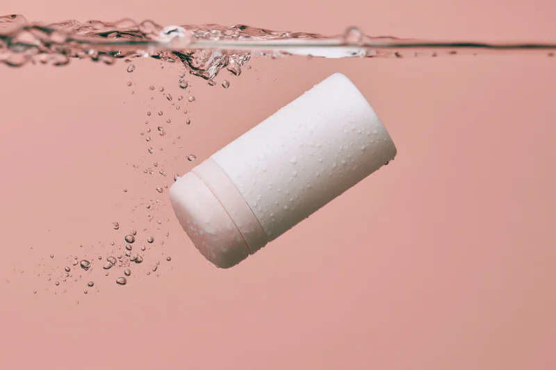 White roll-on deodorant bottle floating just below water surface in pink liquid