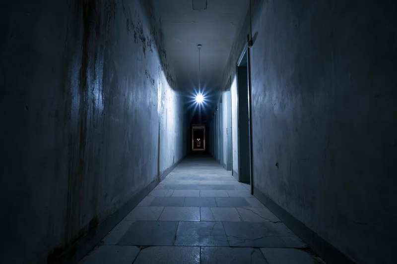 Dimly lit narrow corridor with cracked tiles and peeling walls receding into the distance