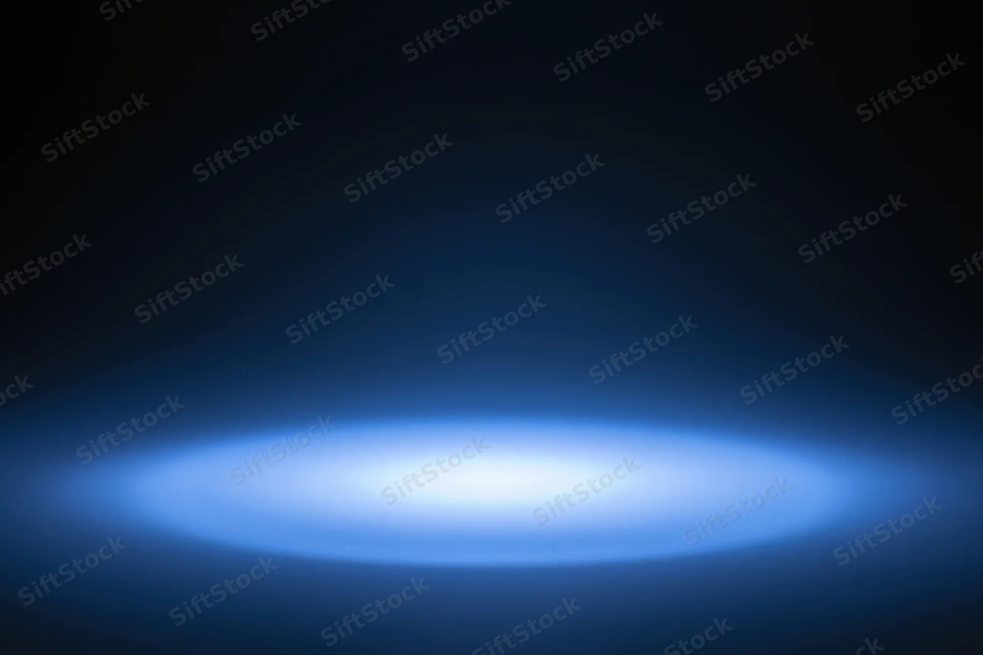 Soft blue radial light glow on dark studio backdrop with central spotlight and copyspace