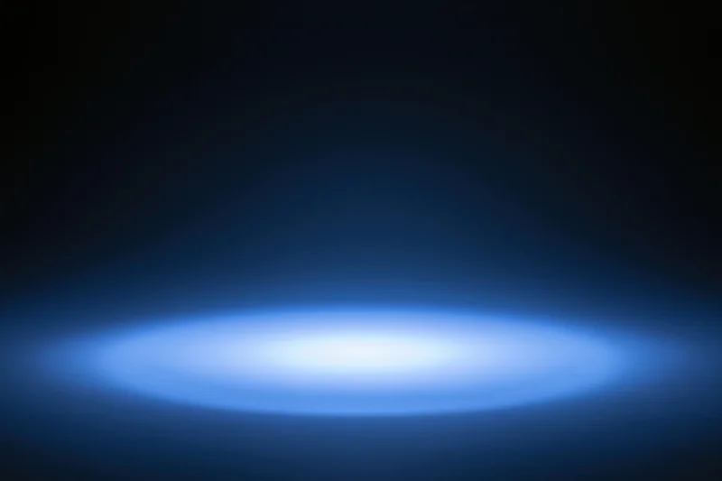 Soft blue radial light glow on dark studio backdrop with central spotlight and copyspace