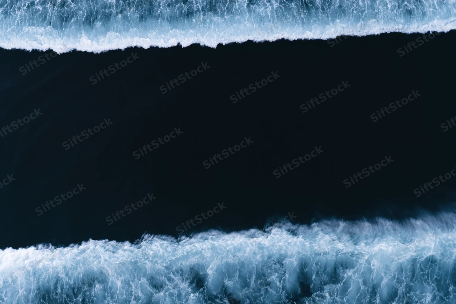 Aerial top-down view of dark ocean water with two bands of white foamy waves at night