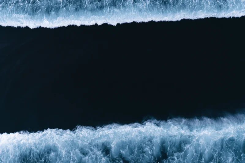 Aerial top-down view of dark ocean water with two bands of white foamy waves at night