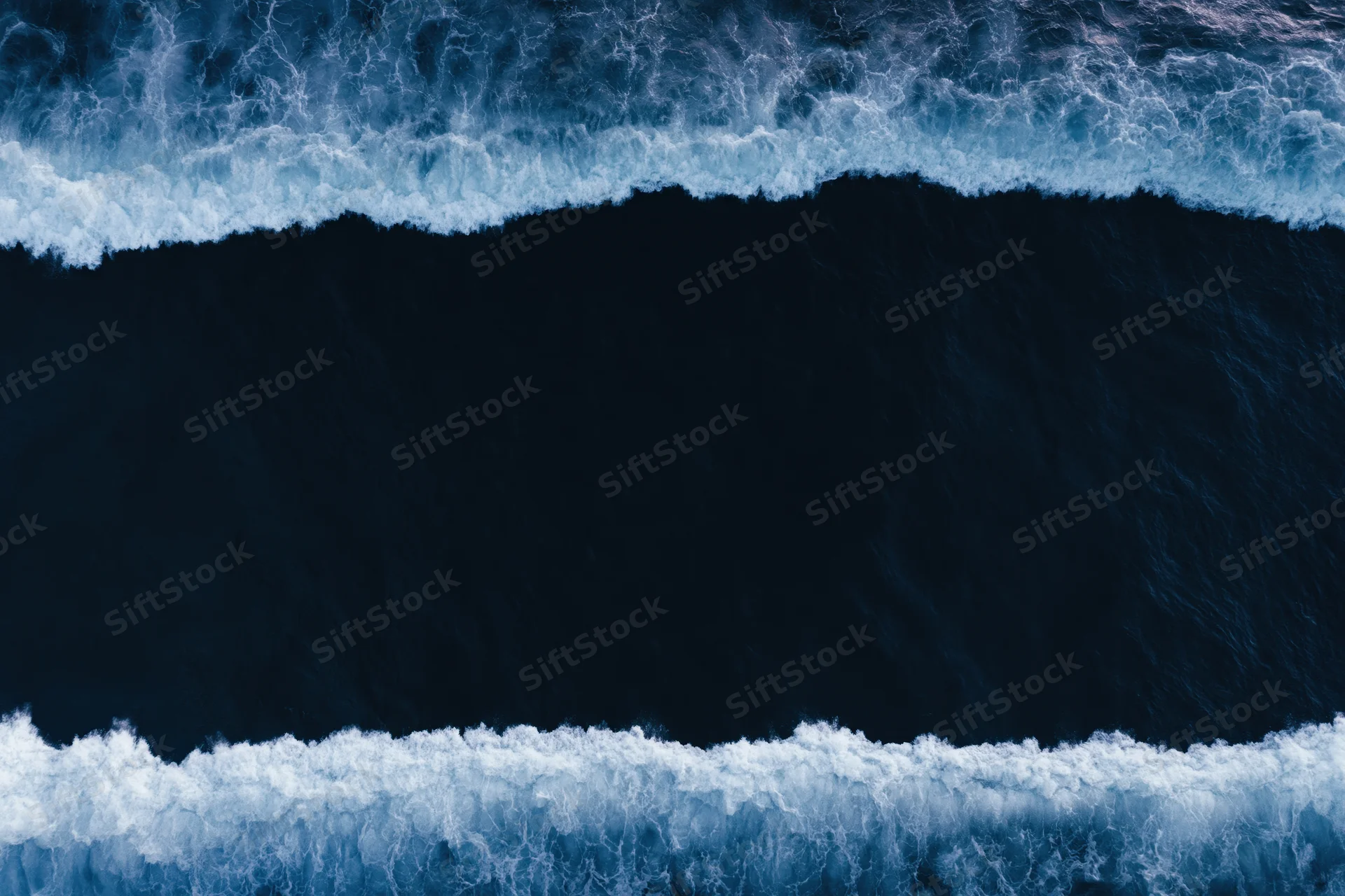 Aerial top-down view of dark ocean waves with white foam bands at night