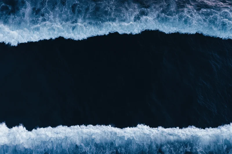 Aerial top-down view of dark ocean waves with white foam bands at night