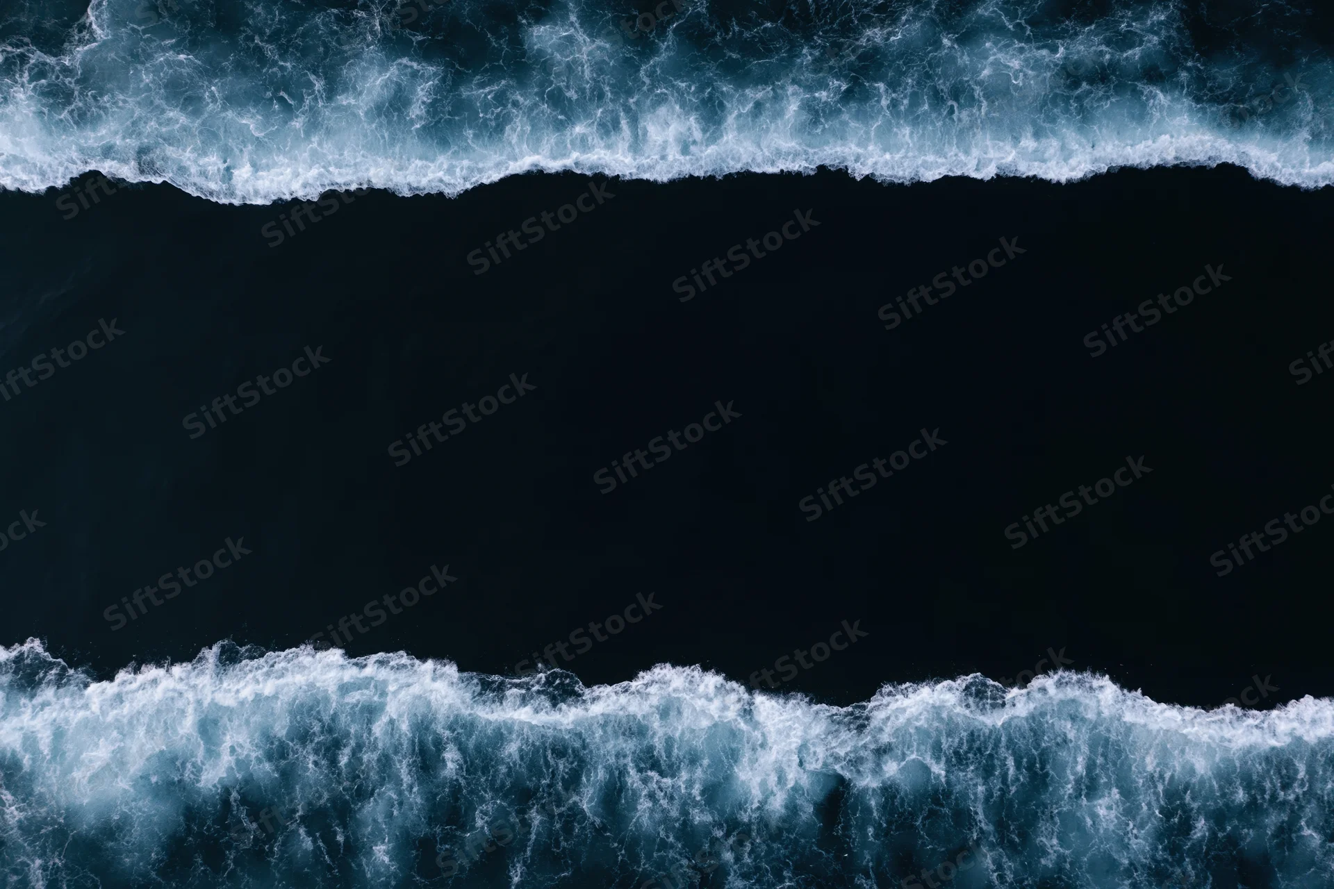 Aerial top-down view of dark ocean waves with white foam bands at night