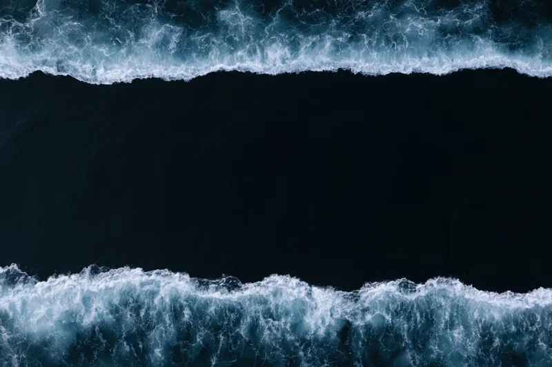 Aerial top-down view of dark ocean waves with white foam bands at night