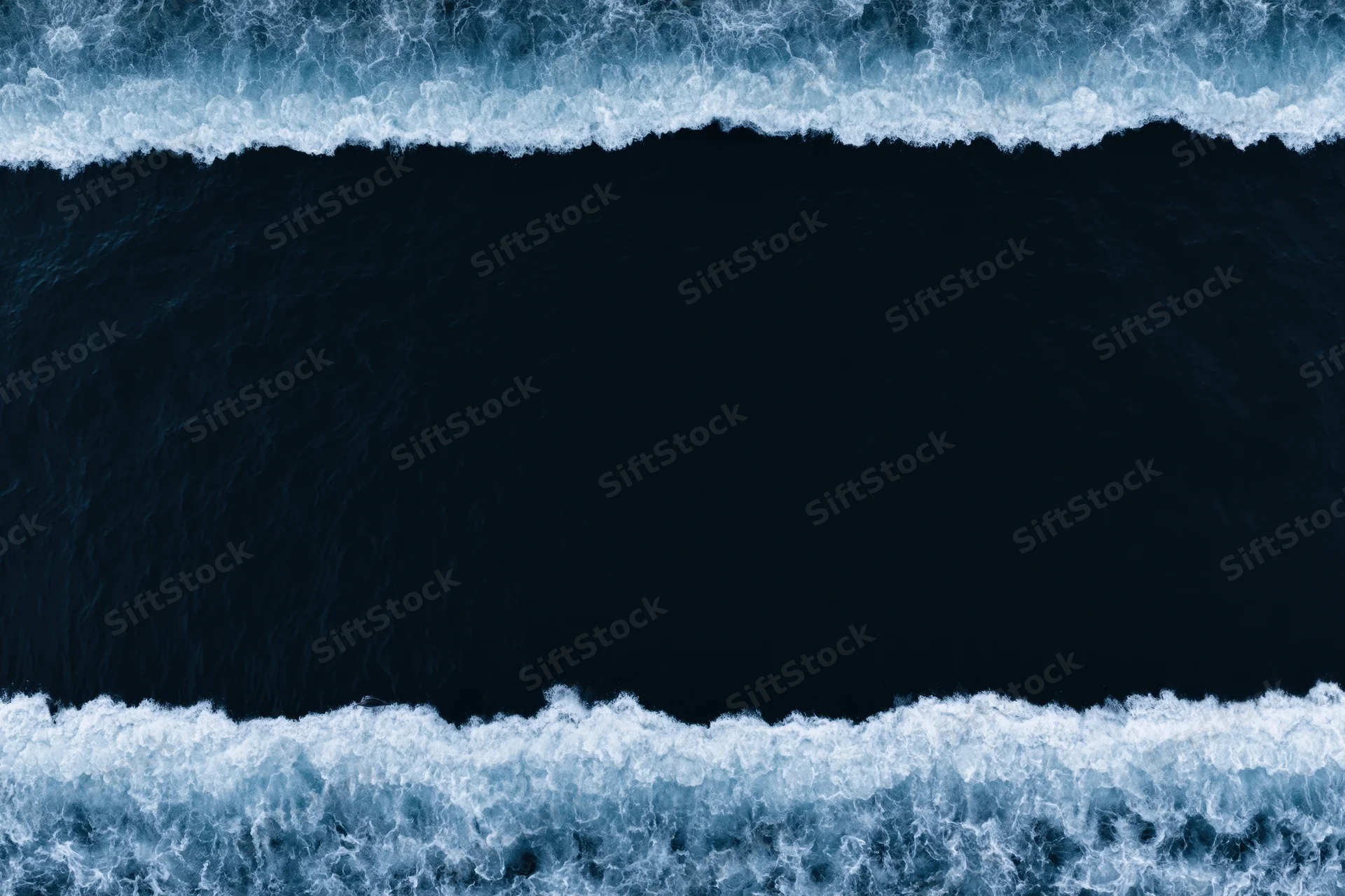 Aerial top-down view of dark ocean waves with white foam bands at night
