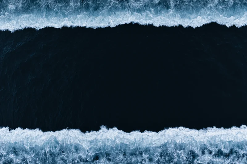 Aerial top-down view of dark ocean waves with white foam bands at night