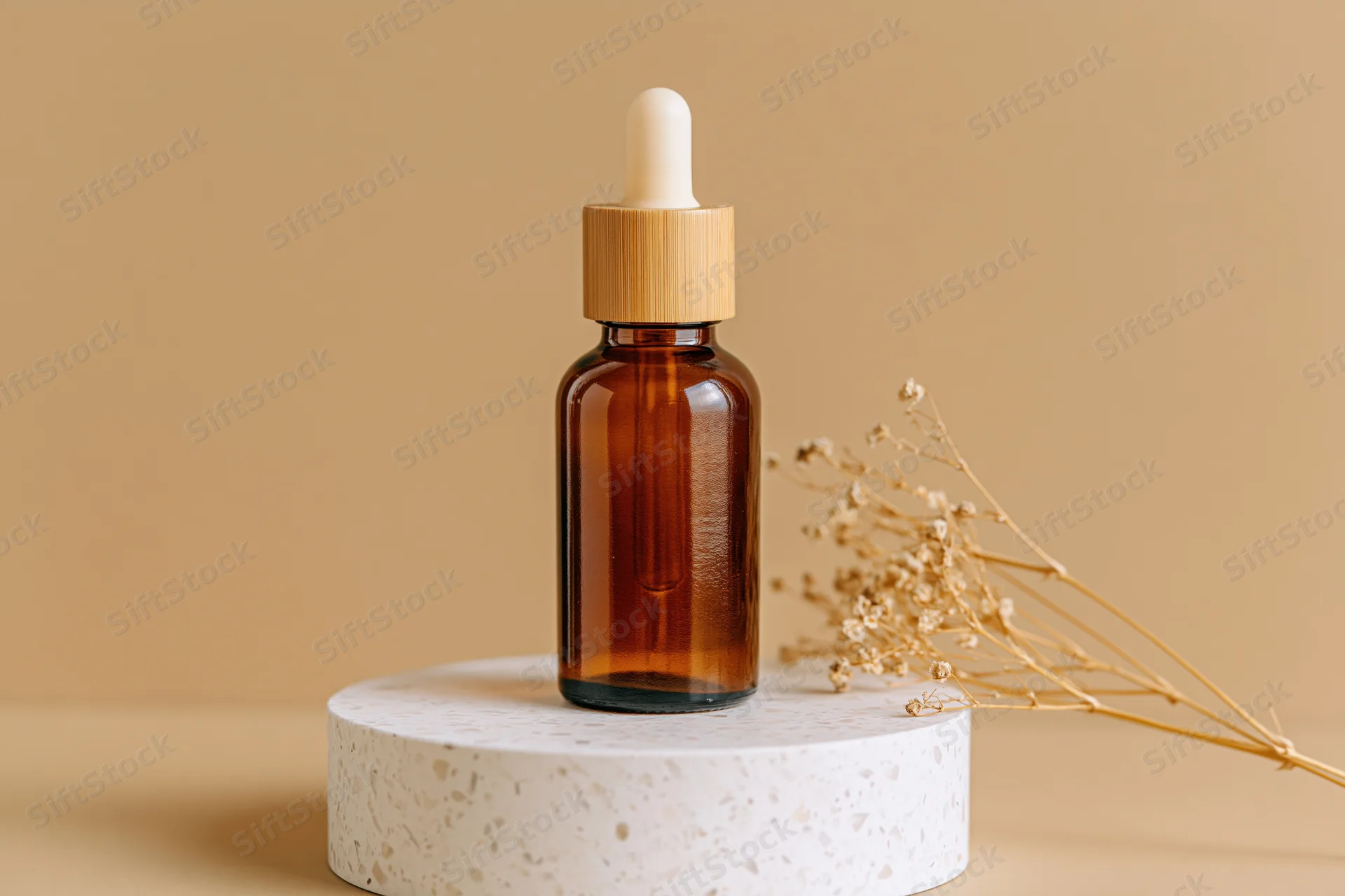 Amber glass dropper bottle with bamboo cap on terrazzo pedestal beside dried flowers