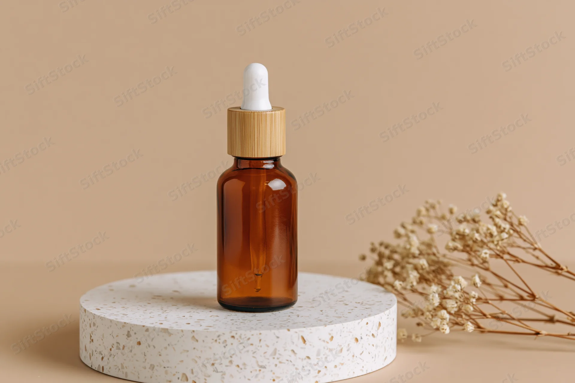 Amber glass dropper bottle with bamboo cap on terrazzo stand beside dried flowers