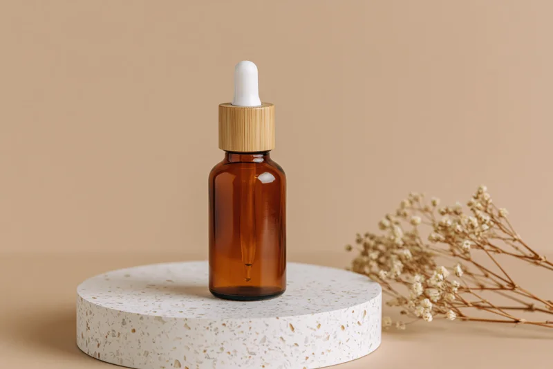 Amber glass dropper bottle with bamboo cap on terrazzo stand beside dried flowers