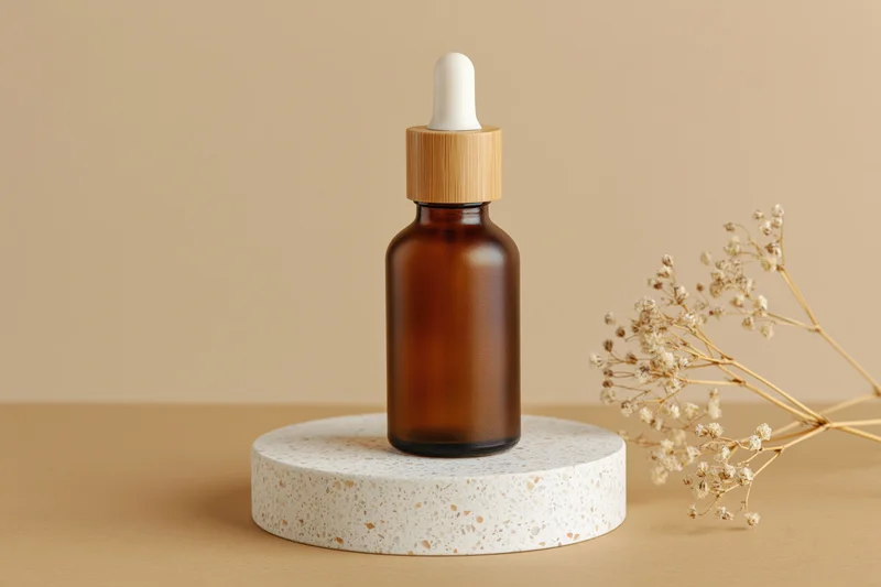 Amber glass dropper bottle with bamboo cap on terrazzo stand beside dried flowers