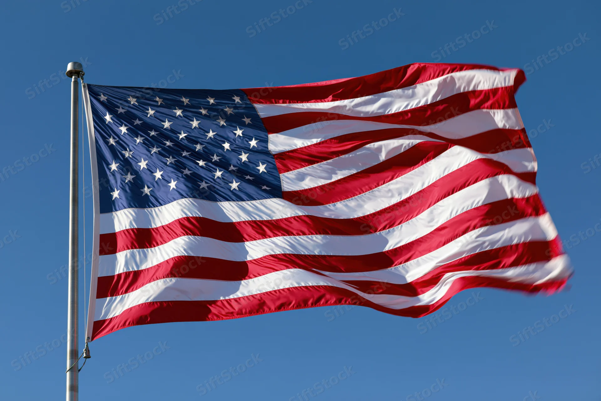 American flag waving in the wind on a metal flagpole against a clear blue sky