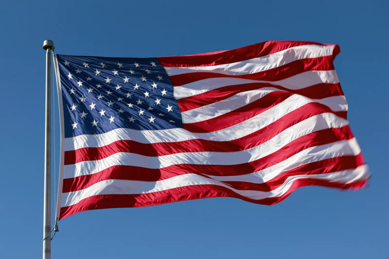 American flag waving in the wind on a metal flagpole against a clear blue sky