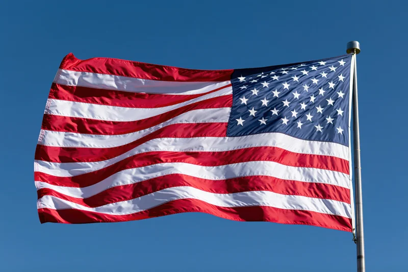 American flag waving in the wind on a metal flagpole against a clear blue sky