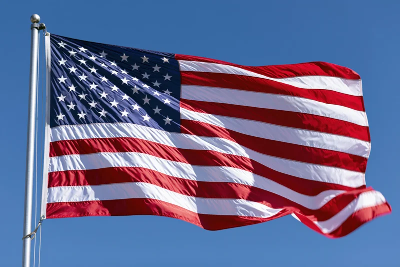 American flag waving in the wind on a metal flagpole against a clear blue sky