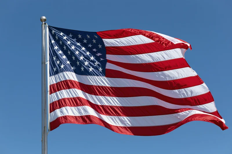 American flag waving in the wind on a metal flagpole against a clear blue sky