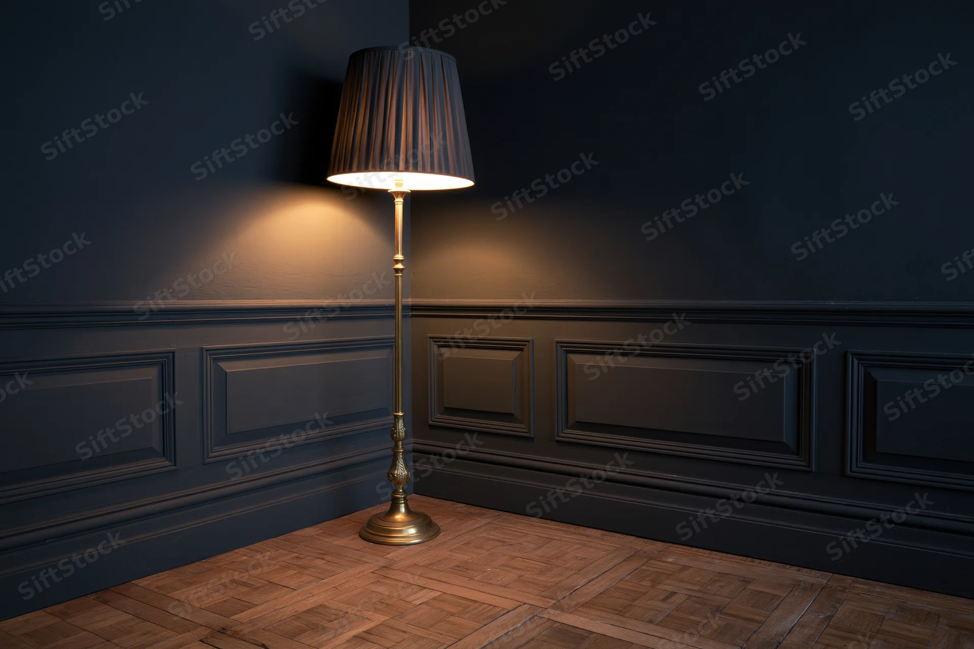Ornate brass floor lamp with dark pleated shade glowing in a dark corner of a room with wainscoting and parquet flooring