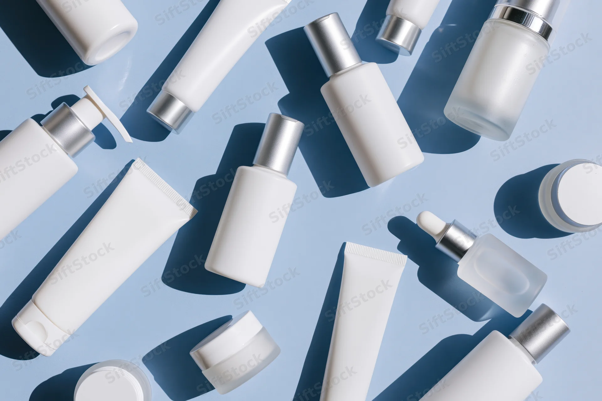 Assorted white skincare bottles and tubes arranged in flat lay on light blue background