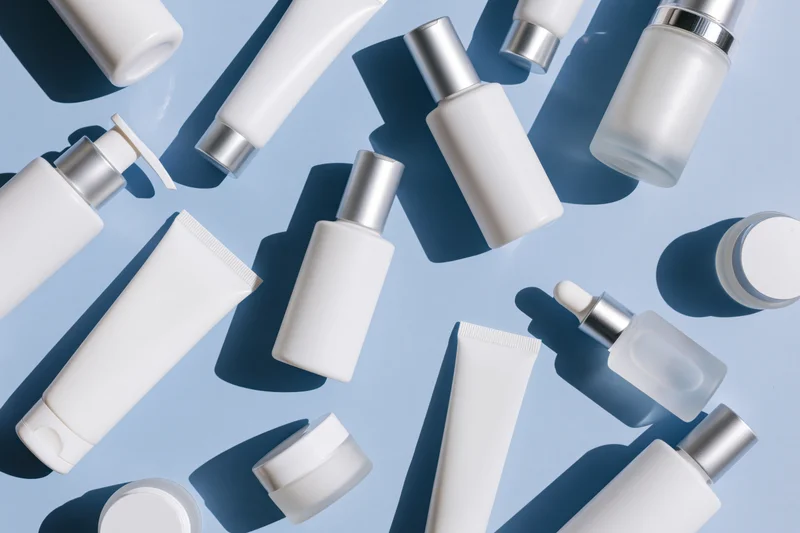 Assorted white skincare bottles and tubes arranged in flat lay on light blue background