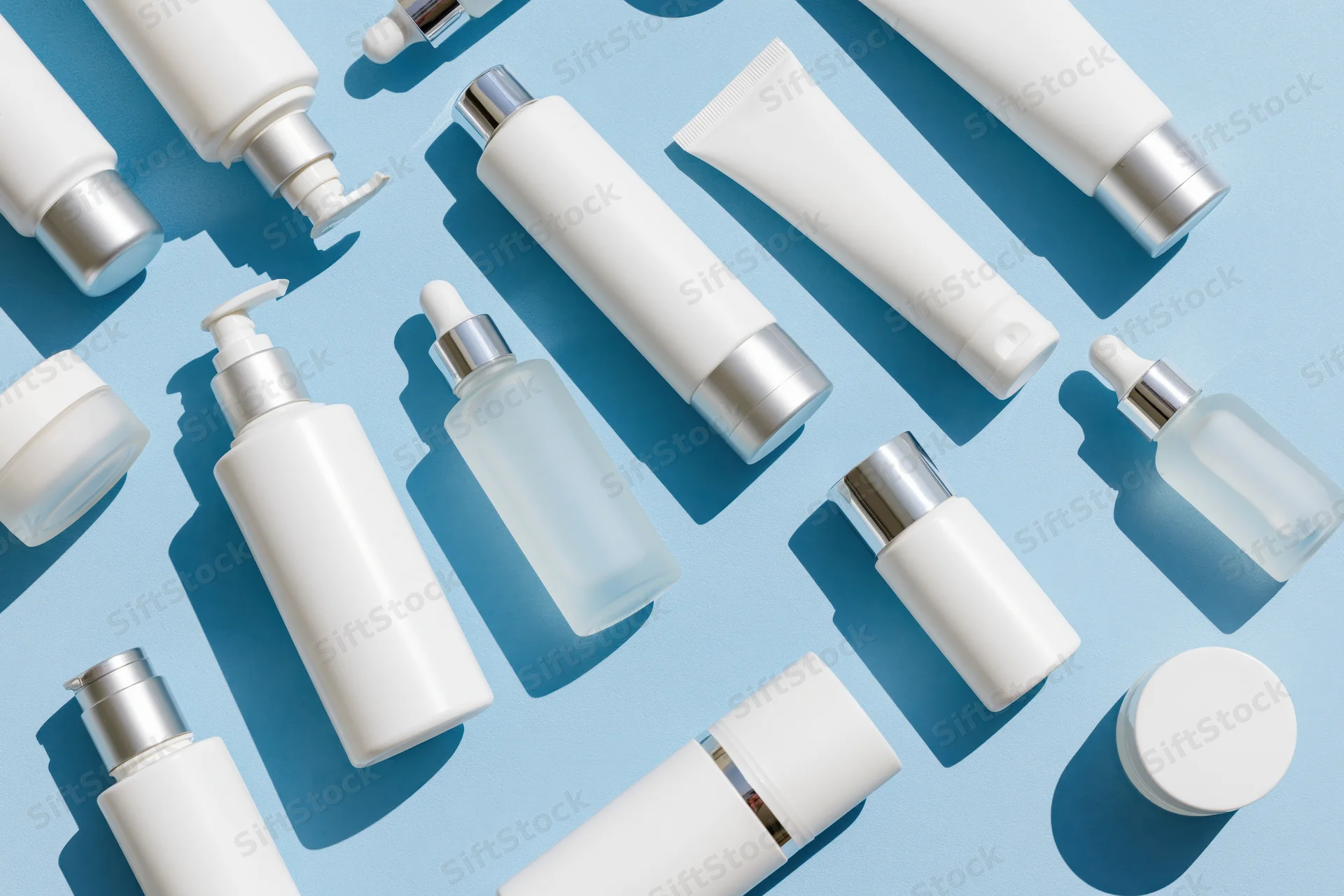 Assorted white skincare bottles and tubes arranged on a blue background