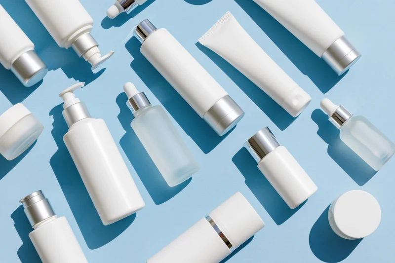 Assorted white skincare bottles and tubes arranged on a blue background