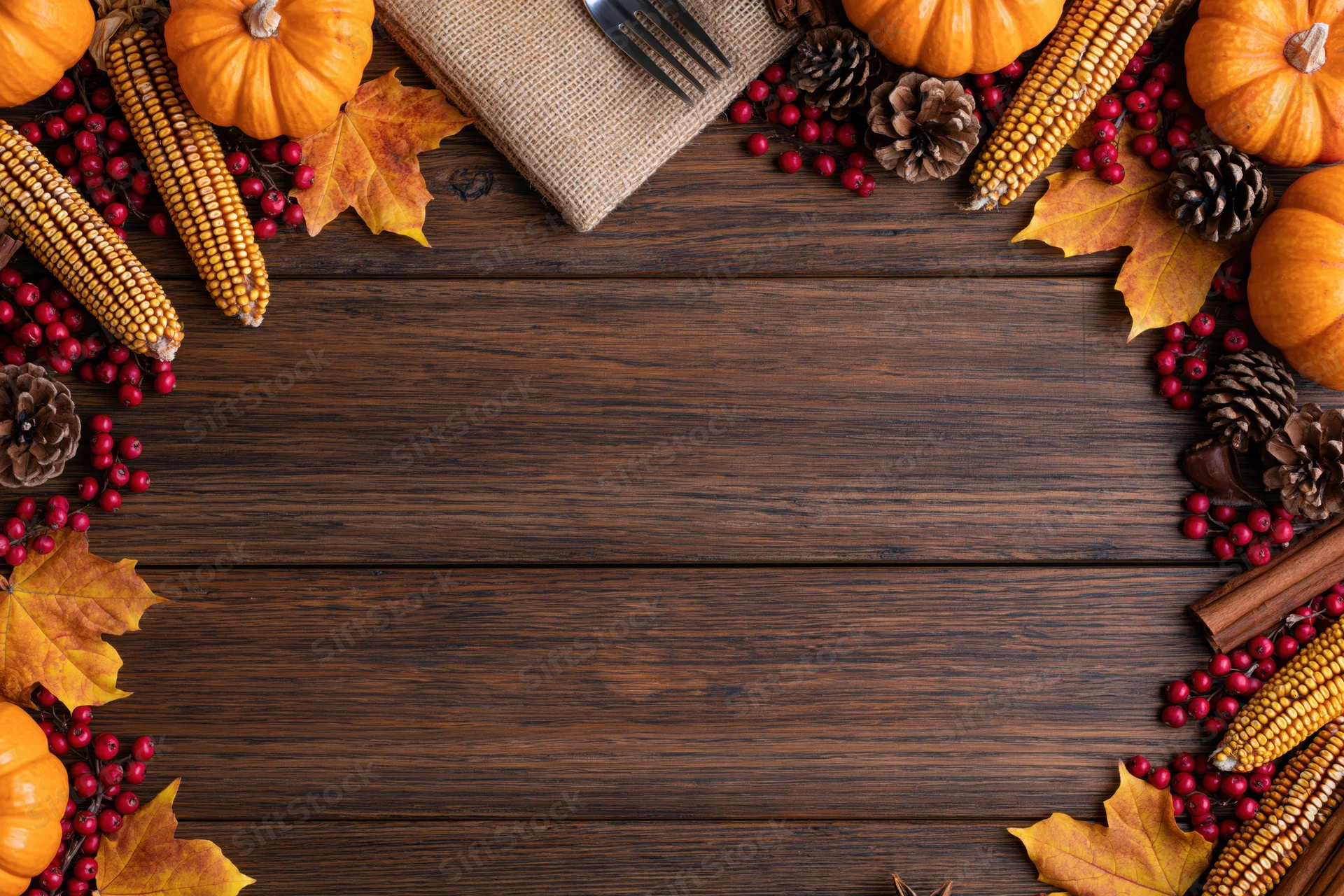Autumn harvest flat lay arrangement on dark wooden table with pumpkins, corn, leaves and berries forming border around central copyspace