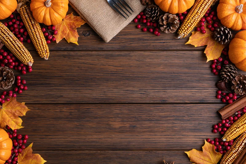 Autumn harvest flat lay arrangement on dark wooden table with pumpkins, corn, leaves and berries forming border around central copyspace