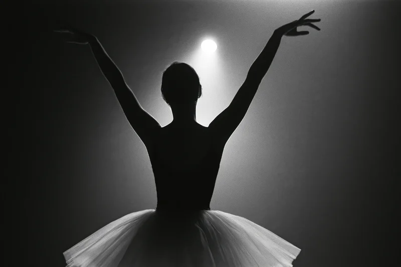 Ballerina silhouette from behind with arms raised overhead under spotlight on stage
