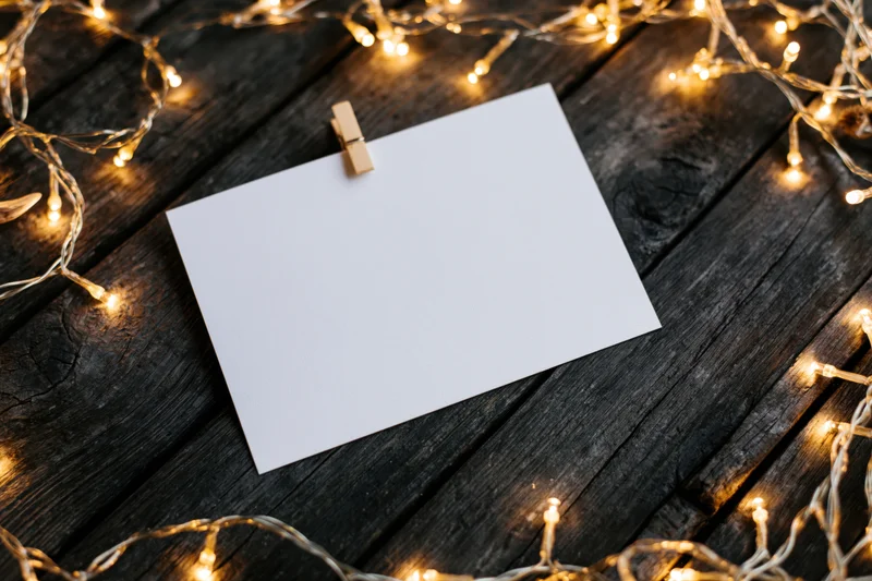 Blank white card clipped with wooden clothespin on dark wood surface surrounded by warm string lights