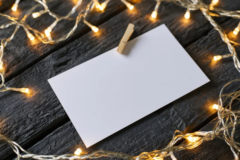 Blank white card clipped with wooden clothespin on dark wood surface surrounded by warm string lights