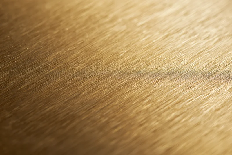 Close-up of brushed gold metal surface with linear texture and warm reflective sheen