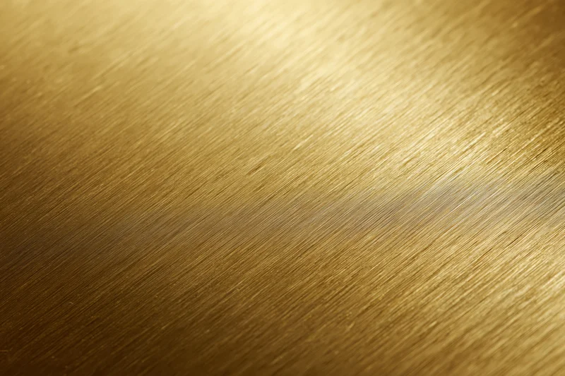 Close-up of brushed gold metal surface with linear texture and warm gradient lighting