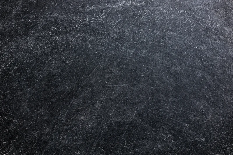Close-up of a dark matte chalkboard surface with scratches and smudges showing texture and wear