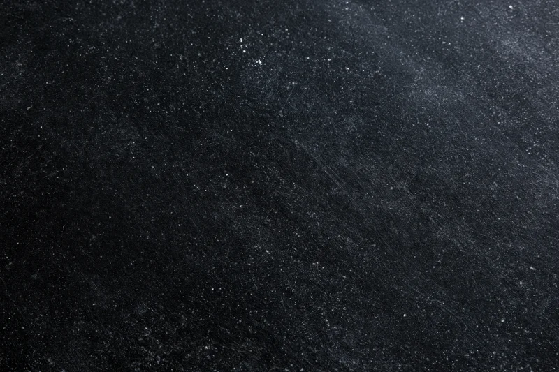 Close-up of a dark matte black chalkboard surface with fine texture and scattered white specks