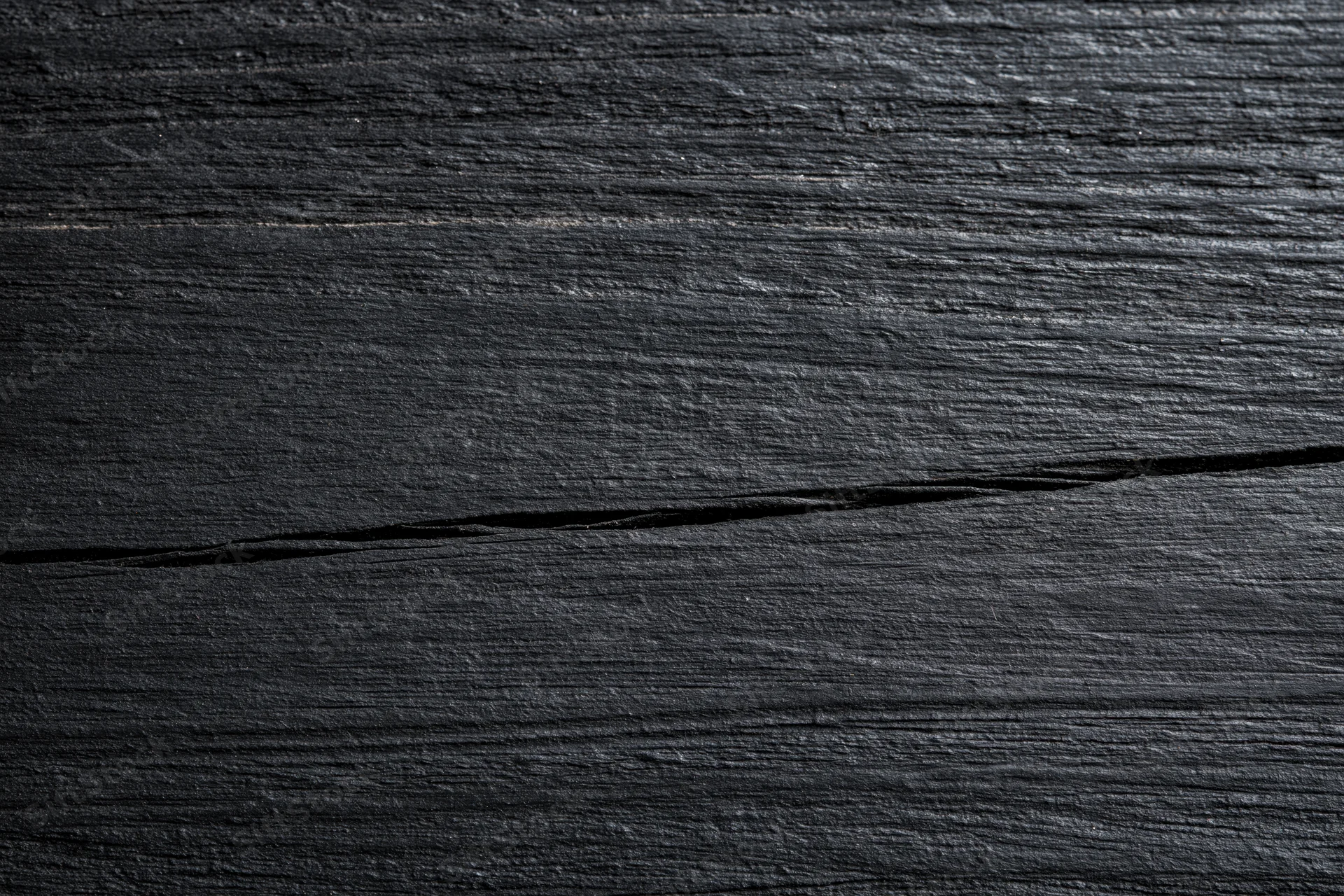 Close-up of dark black wooden surface with visible grain and crack, flat lay view