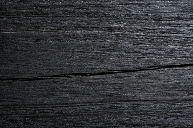 Close-up of dark black wooden surface with visible grain and crack, flat lay view