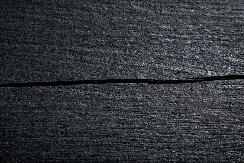 Close-up of dark black wooden surface with horizontal crack and visible grain pattern