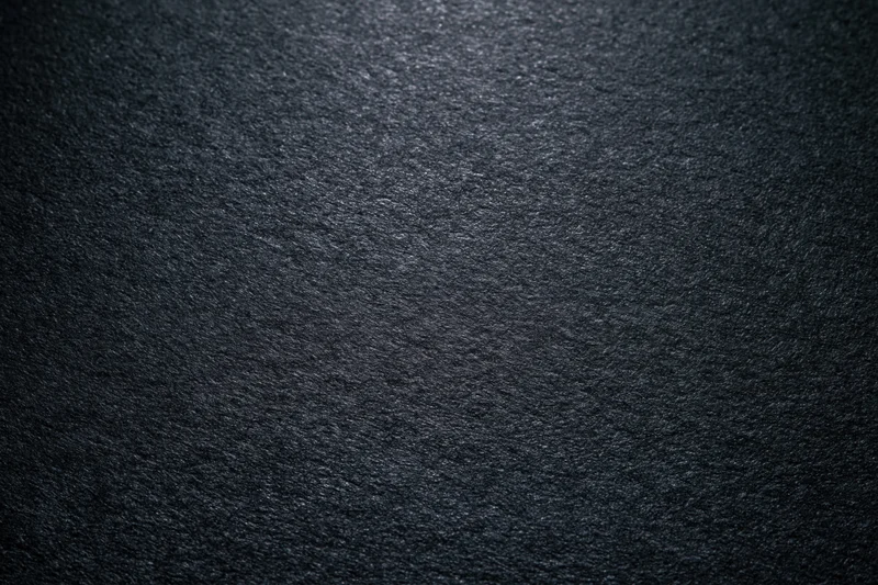 Close-up of dark charcoal matte paper surface with textured grain and soft lighting gradient