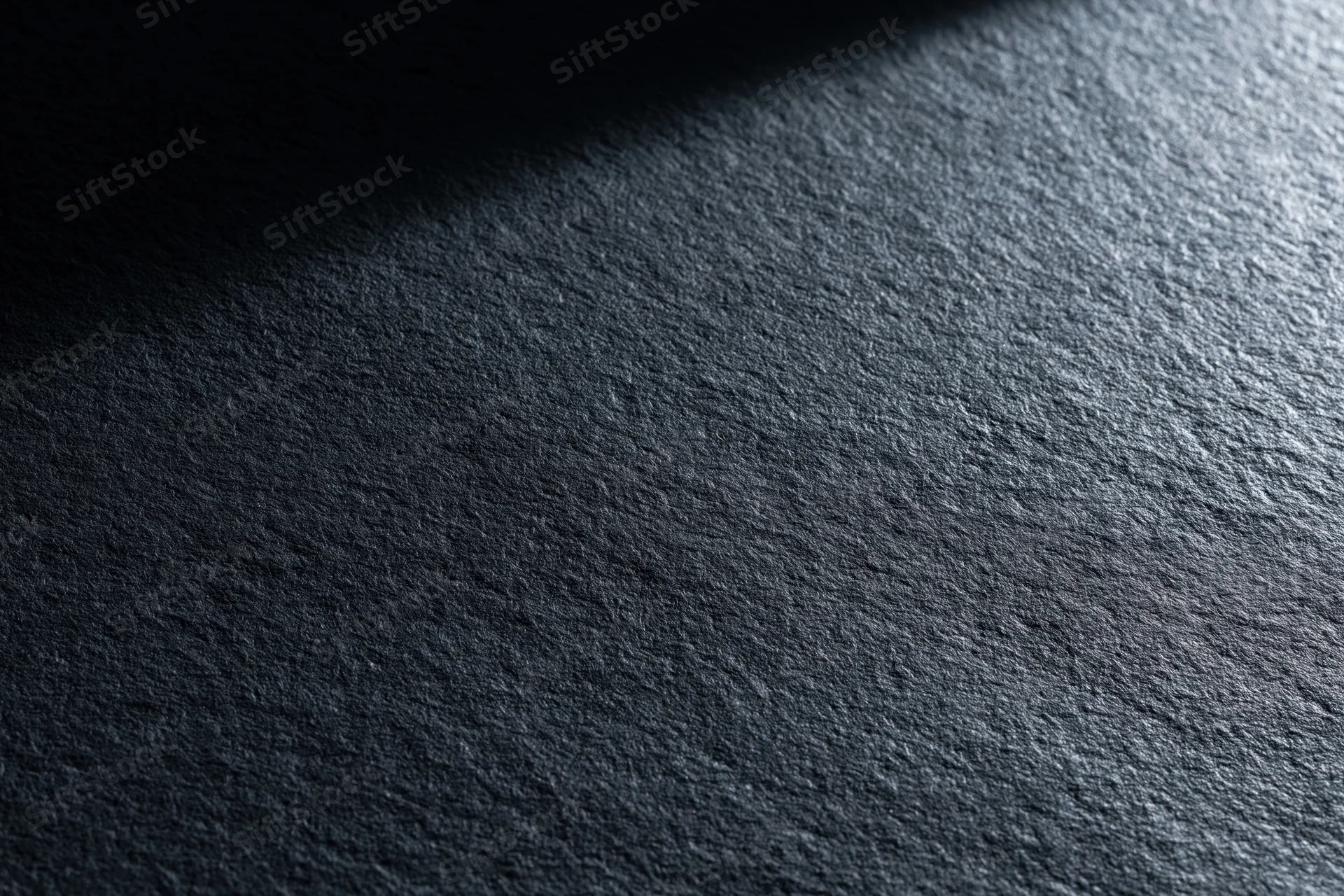 Close-up of dark matte textured surface with light and shadow gradient