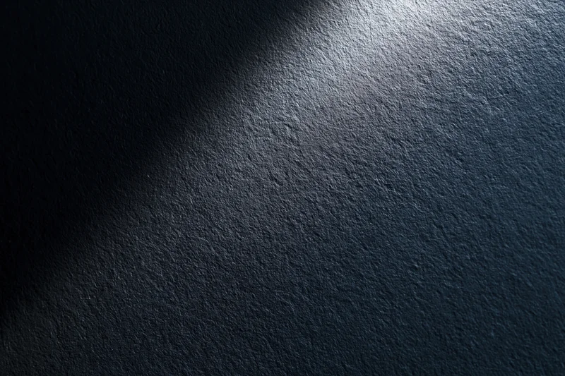 Dark matte textured surface with spotlight gradient and shadowed edges