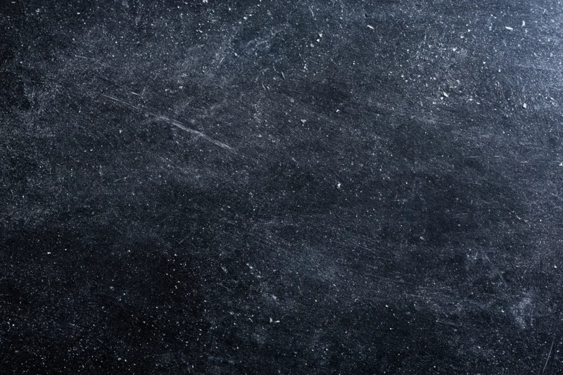Close-up of a dark scratched chalkboard surface with white residue and texture