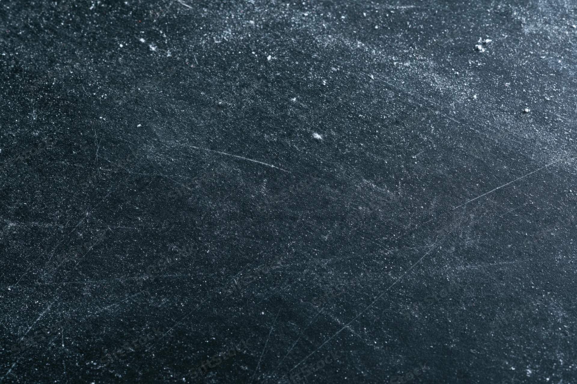 Close-up of a dark scratched chalkboard surface with dust and faint marks
